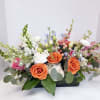 Low floral arrangement with orange and white roses in a black container