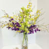 Tall orchid arrangement in a clear glass vase with yellow and purple blooms