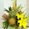 Yellow lilies and a protea in a vase with mixed greenery