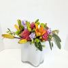 Mixed bouquet of pink roses, orange lilies, and purple flowers in a white vase