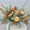 Orange roses and dahlias in a low vase with airy dried grasses