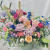 Large mixed floral arrangement in a pale green vase with pink, peach, blue, and lavender blooms.