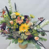 Large mixed floral arrangement in a tan vase with bright yellow and peach blooms