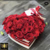 Heart-shaped box filled with red roses and topped with a red ribbon and card
