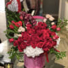 Round arrangement of red roses, tulips, orchids and white hydrangeas in a pink box with a heart balloon