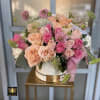 Round hatbox of peach and pink roses with filler blooms on a gold metal stand