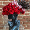 Black sculptural face vase topped with red roses, pink orchids, and dark wispy accents.