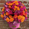Round arrangement of hot pink and orange roses with purple alstroemeria in a pink hatbox