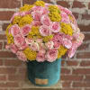 Round hatbox arrangement of pink roses and yellow filler blooms in a teal container
