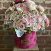 Round arrangement of blush and ivory roses and ranunculus in a pink velvet hatbox.