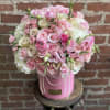 Round arrangement of pale pink and cream roses in a pink hatbox with pearl garlands.