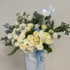 Large arrangement of cream roses and white flowers with blue ribbons and a stork pick in a white vase.