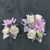Two lavender and white floral corsages on a dark fabric background