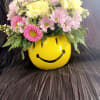 Pink and yellow daisy bouquet in a yellow smiley-face container