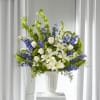White lilies and roses arranged with blue flowers in a white vase.