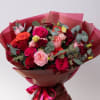 Bouquet of pink, red, and orange roses wrapped in burgundy paper