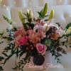 Pink lilies and roses arranged in a pale hatbox with greenery