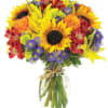 Bright mixed bouquet with sunflowers, roses, and purple daisies in a glass vase