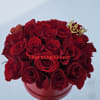 Red roses arranged in a round red box with a small crown decoration