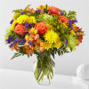 Bright mixed bouquet of roses, daisies, and purple accents in a glass vase