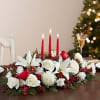 Holiday centerpiece with white flowers, red candles, and pinecones on a table