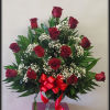 Red roses arranged in a clear vase with baby's breath and a red ribbon