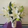 White lilies arranged in a white vase with a cross emblem