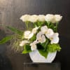 Modern white arrangement of roses and orchids in a white vase with bold green accents.