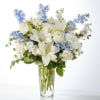 White lilies and roses in a clear glass vase with blue flowers