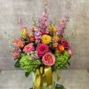 Colorful bouquet of pink, orange, and yellow flowers in a green box with a gold ribbon
