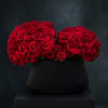 Two dense red rose bouquets in a black vase on a pedestal