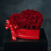 Red roses arranged in a red heart-shaped box with a ribbon bow