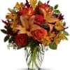 Orange roses and lilies in a clear glass vase with red and yellow accents