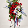 Standing floral spray with red carnations, white lilies, and blue flowers on an easel