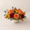 Orange roses and red carnations in a white vase with autumn leaves