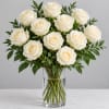 White roses arranged in a clear glass vase with greenery