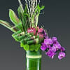 Tall floral arrangement with purple orchids in a green vase