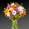 Mixed bouquet of roses, lilies, daisies, and sunflowers in a clear glass vase