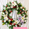 Large floral wreath with white lilies, daisies, and red roses on a stand