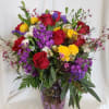 Mixed bouquet of red, yellow, and purple flowers in a purple glass vase