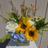 Bouquet of sunflowers, white roses, and blue hydrangea in a glass vase