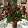 Red roses arranged in a tall black vase with baby's breath and a red ribbon