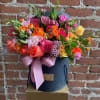 Mixed bouquet of roses and small filler flowers in a dark hatbox with a pink ribbon