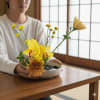 Person holding a small yellow flower arrangement in a bowl