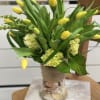 Yellow tulips and pale green hydrangeas in a glass vase wrapped with burlap