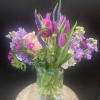 Mixed bouquet of purple tulips, pink roses, and lavender flowers in a glass vase