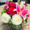 Bouquet of pink lilies, red roses, and white blooms in a glass vase