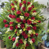 Tall standing spray of red roses with white flowers and yellow accents on lush greenery.
