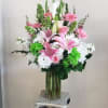 Pink lilies and white flowers arranged in a glass vase on a pedestal