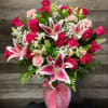 Pink roses and lilies arranged in a glass vase with a ribbon.